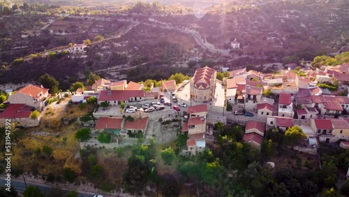 Aerial drone sunset footage of traditional countryside hilltop village Vouni, in Limassol, Cyprus. 360 view of christian church Ioannis Prodromos, ceramic tiled roof houses, narrow streets from above.