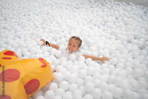 Happy little girl playing white plastic balls pool in amusement park. playground for kids. photo