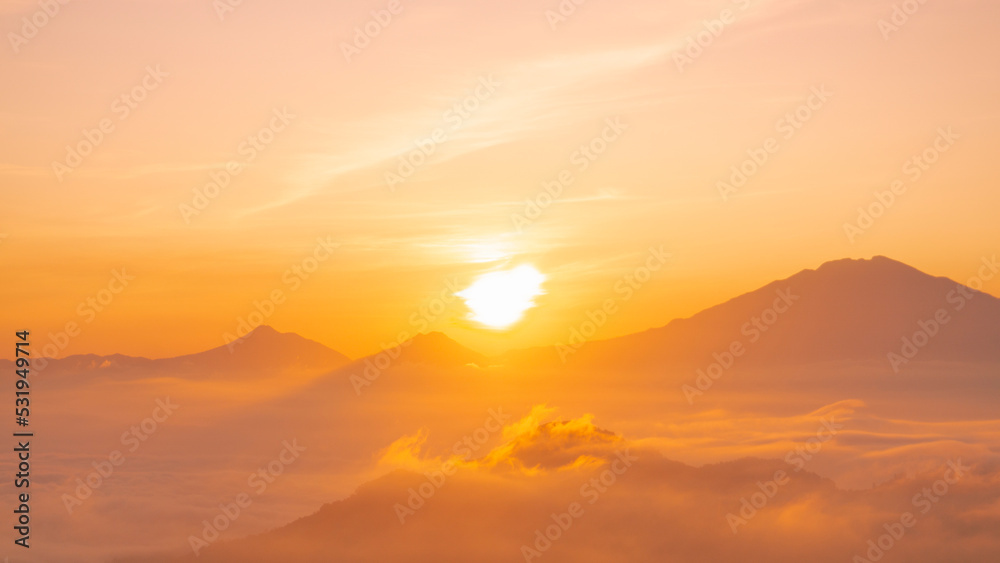 Golden sunrise over white puffy clouds with distant mountains on horizon