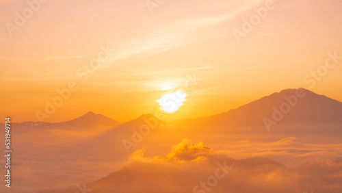 Golden sunrise over white puffy clouds with distant mountains on horizon