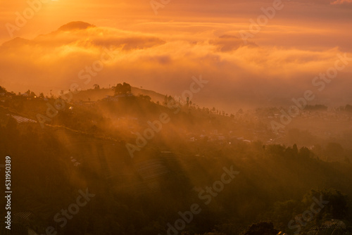 Golden sunrise over white puffy clouds with distant mountains on horizon. Sun ray through the mist in the mountains