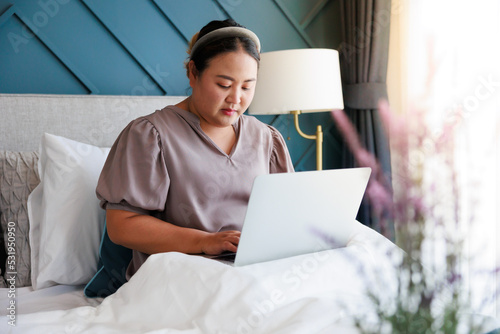 Asian woman working on laptop at home on the bed through internet for her business.