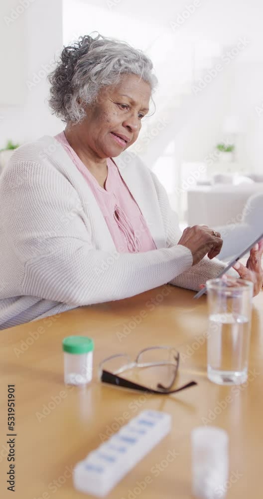 Vertical video of senior african american woman sitting at table, taking pills Vertical video of senior african american woman sitting at table, taking pills