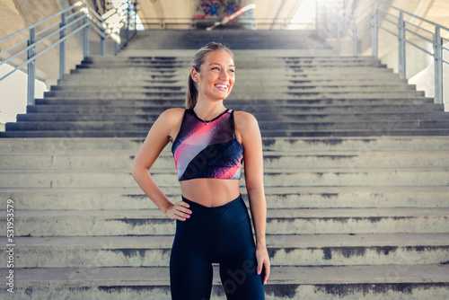 Portrait shot of a smiling young blond woman standing in front of a set of stairs before working out.