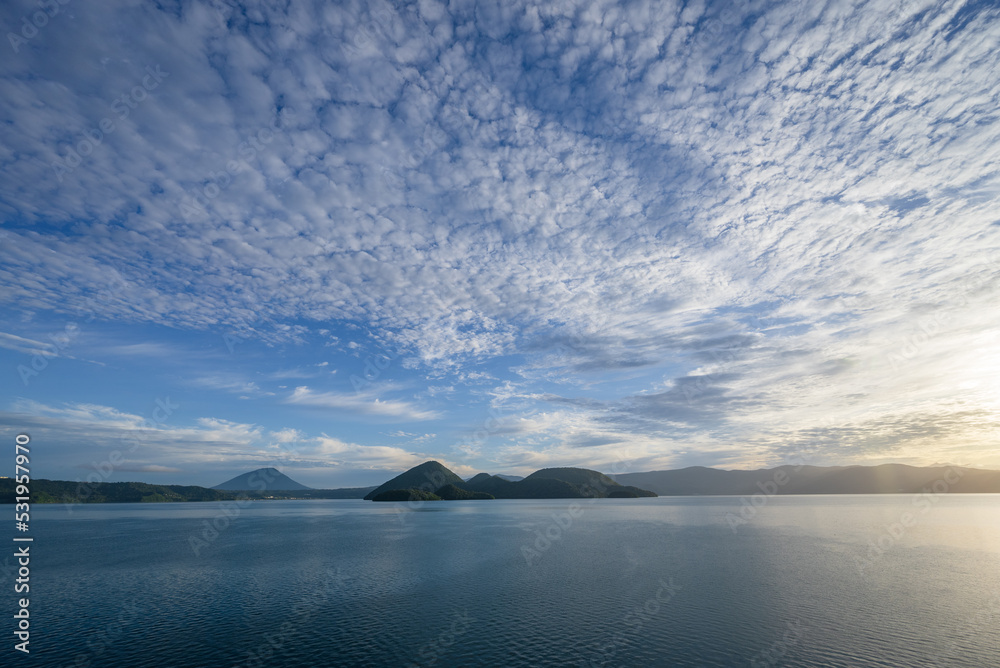 青空と流れゆく白い雲と朝日を映す洞爺湖面