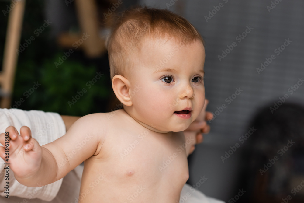 mother supporting curious infant daughter looking away in bedroom. mother supporting curious infant daughter looking away in bedroom.