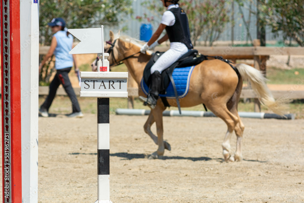 Close up on Start Signage on Blurred girl that rides a Pony during Pony Game Competition Close up on Start Signage on Blurred girl that rides a Pony during Pony Game Competition