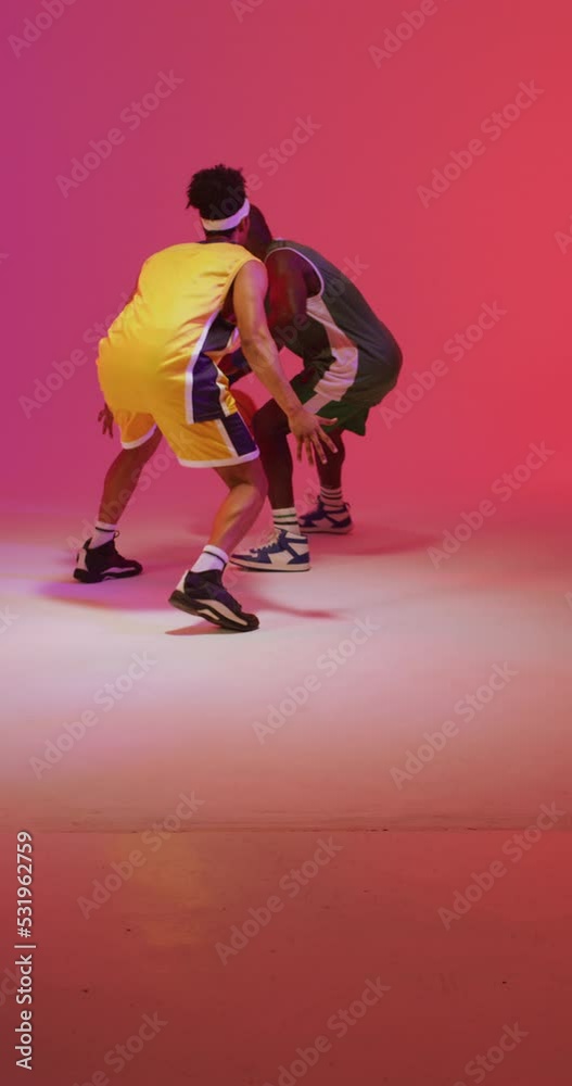 Vertical video of two diverse male basketball players playing with ball on pink background Vertical video of two diverse male basketball players playing with ball on pink background