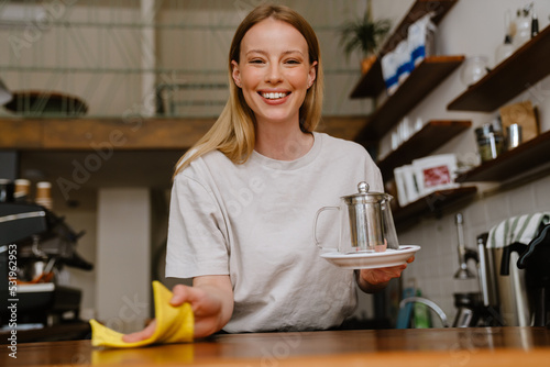 Blonde white barista woman smiling while cleaning counter in cafe © Drobot Dean