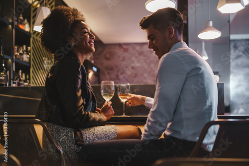Romantic couple on a date talking holding a glass of white wine sitting at the bar counter in the night