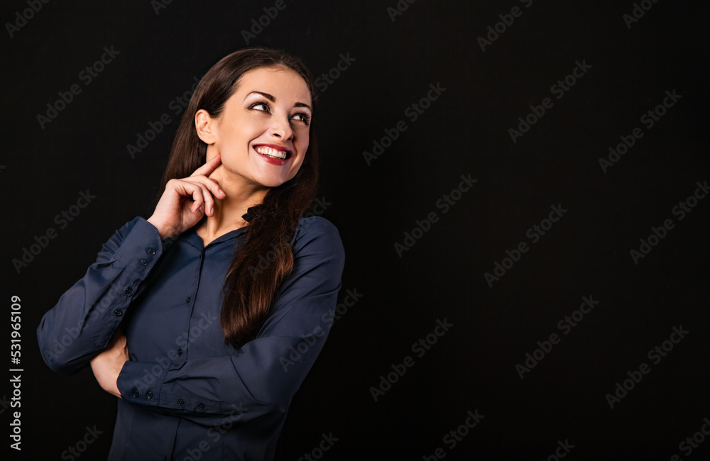 Beautiful thinking toothy smiling business woman looking up with folded arms in blue shirt on black background with empty copy space for text. Closeup Beautiful thinking toothy smiling business woman looking up with folded arms in blue shirt on black background with empty copy space for text. Closeup