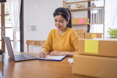 Business Asian women working on laptop computer checking customer order online shipping box at home. Starting Small business entrepreneur SME freelance. Online business, Work at home SME concept.