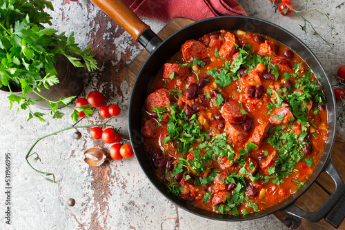 frying pan with stewed beans with sausages in tomato sauce on the table photo