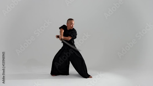 Japanese man traditional dress, black kimano katana samurai sword strikes, takes out scabbard, holds handle, trains kenjutsu, practices techniques, sword training combat principles samurai fighting