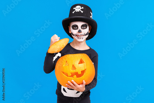 Happy cheerful boy in skeleton costume with  pumpkin  jack-o-lantern celebrates Halloween and laughs on blue background