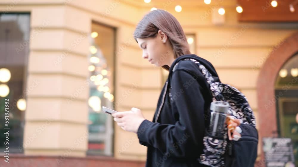Teenage girl walking with smartphone in urban street. Girl typing by mobile phone outdoors Teenage girl walking with smartphone in urban street. Girl typing by mobile phone outdoors