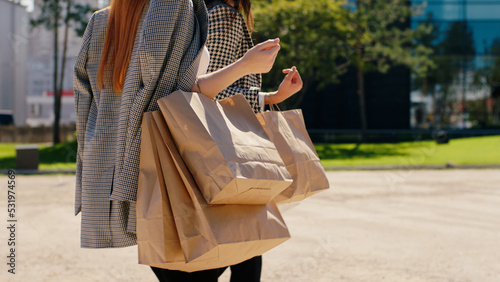In the middle of modern town two charismatic and attractive women with some eco shopping bags walking together and discussing