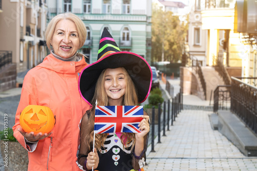 Grandmother and granddaughter with UK flag, near the house on the day of Halloween. Little girl in a witch costume.