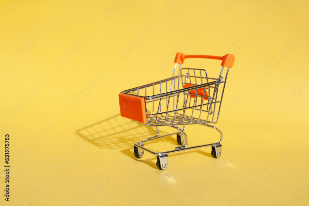 Small supermarket grocery push cart for shopping. Shopaholic. Buyer. Shopping concept. Close-up. Isolated shopping trolley on a yellow background. Copy space. Small supermarket grocery push cart for shopping. Shopaholic. Buyer. Shopping concept. Close-up. Isolated shopping trolley on a yellow background. Copy space.