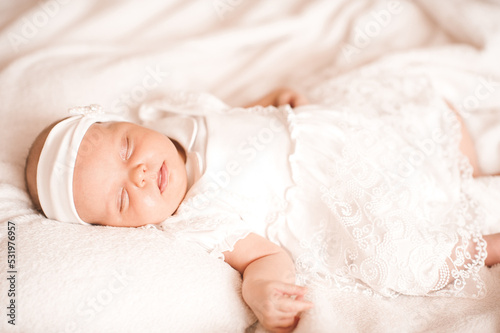 Sleeping cute baby infant girl wear stylish white dress and headband in bed.