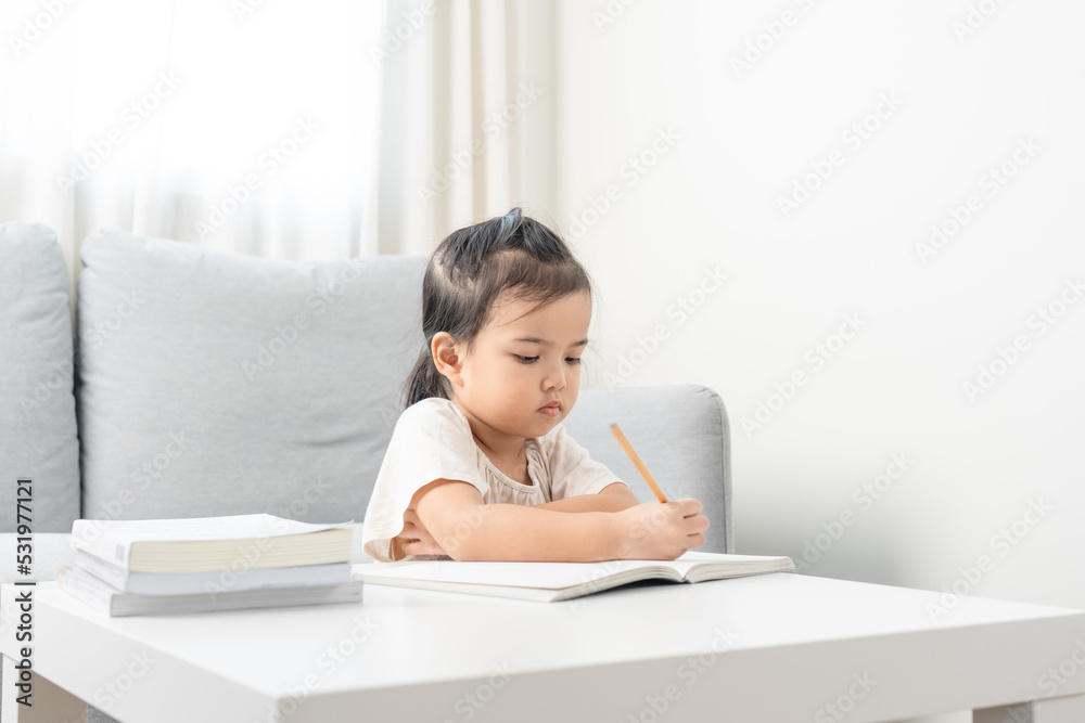 Little girl doing homework using pencil. Asian girl writing on book for education. Little girl doing homework using pencil. Asian girl writing on book for education.