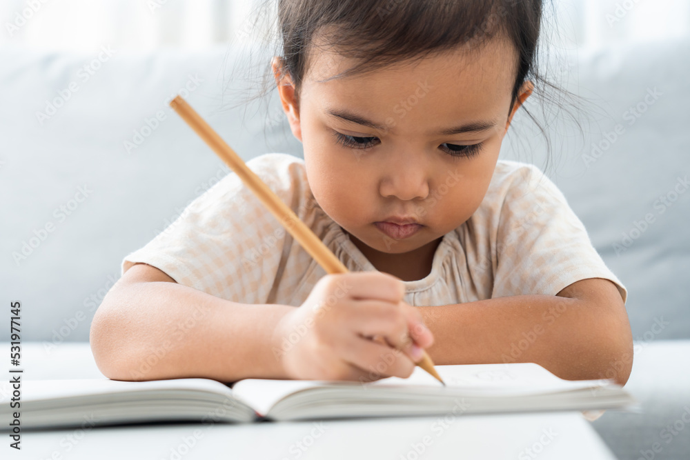 Little girl doing homework using pencil. Asian girl writing on book for education. Little girl doing homework using pencil. Asian girl writing on book for education.