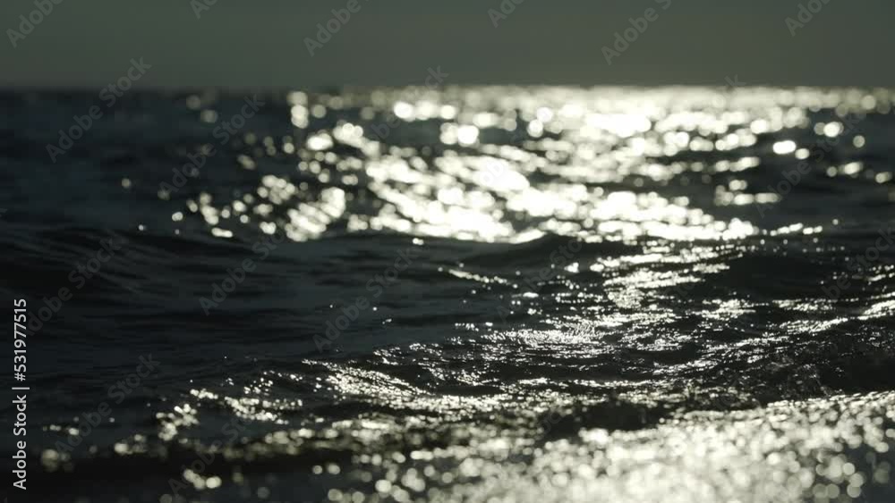 Bokeh of bright blurred orange glare from the sun on the sea water surface. Abstract slow-motion shot
