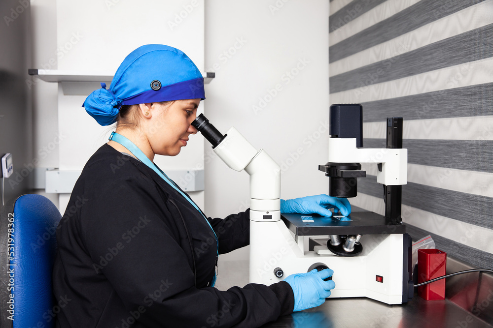 Female scientist looking at slides with patient samples using an inverted microscope in the laboratory.