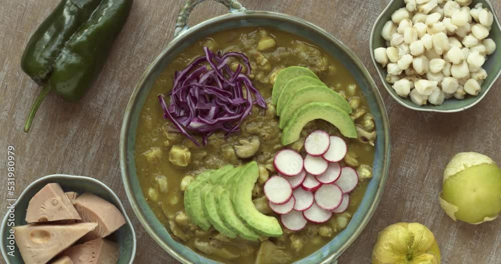 Vegan Pozole verde topped with sliced avocado, radish and red cabbage with raw ingredients: hominy, poblano pepper, fresh tomatillo, jackfruit and shiitake mushrooms. Table spin.