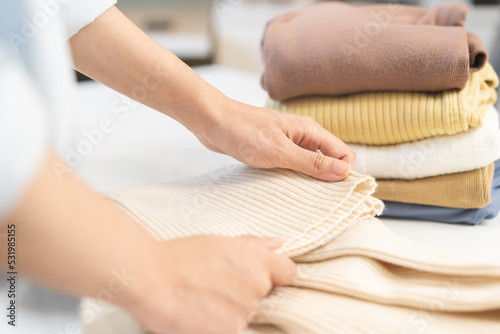 Housewife, asian young woman hand in many folding freshly shirts, sweaters or dress on desk, table after washing clean clothes and drying, making household working in room at home. Laundry and maid.