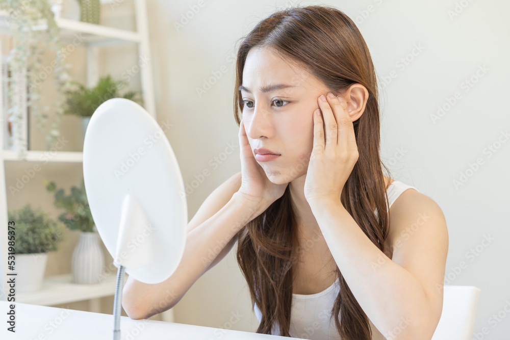 Dermatology, puberty asian young woman, girl looking into mirror, allergy presenting an allergic reaction from cosmetic, red spot or rash on face. Beauty care from skin problem by medical treatment. Dermatology, puberty asian young woman, girl looking into mirror, allergy presenting an allergic reaction from cosmetic, red spot or rash on face. Beauty care from skin problem by medical treatment.