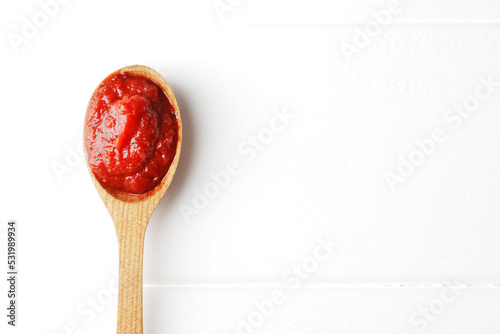 A spoon full of tomato sauce on a white wooden background with space for text. Ingredient Tomato Sauce for Cooking
