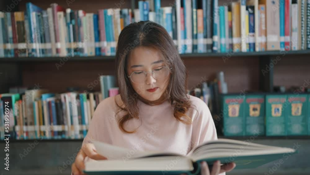 Asian woman student wearing glasses reads books for class assignments and exam preparations in university library. Asian woman student wearing glasses reads books for class assignments and exam preparations in university library.