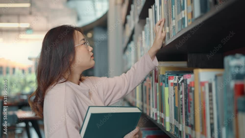 Asian student looking at rows of bookshelves searching for class assignments and exam preparations in the university library. Asian student looking at rows of bookshelves searching for class assignments and exam preparations in the university library.