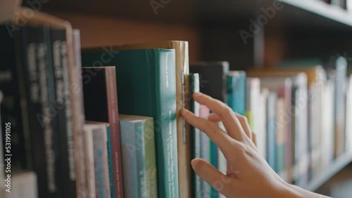 Close-up of hand female pulling book from bookshelf in public library in university, college or high school.