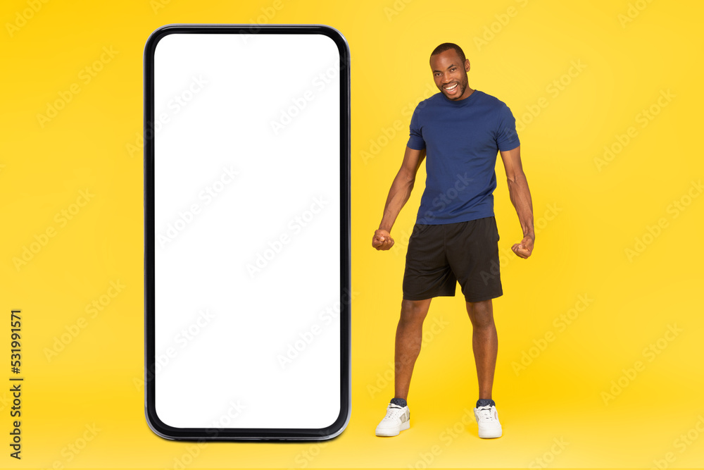 Sporty African Man Posing Near Huge Phone Screen, Yellow Background Sporty African Man Posing Near Huge Phone Screen, Yellow Background