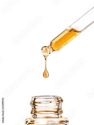 Cosmetic pipette with yellow oily drop close up, isolated on white background. Beauty drop of luxurious gold oil or oily serum dripping from glass pipette in bottle, isolated on white background photo
