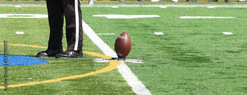 Photography Football on the tee for kickoff with thr referee standing next to the ball