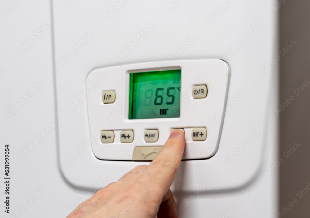 A person regulating the heating temperature by pressing buttons on the boiler for saving A person regulating the heating temperature by pressing buttons on the boiler for saving