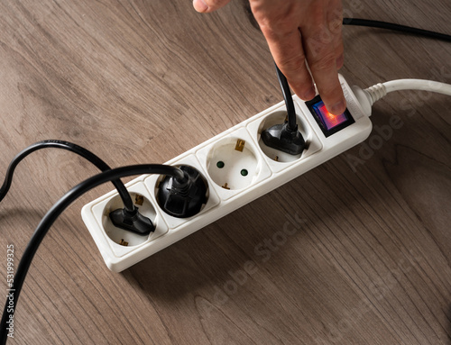 A man cutting off the electrical current by turning off the button on a white electrical socket to reduce energy consumption
