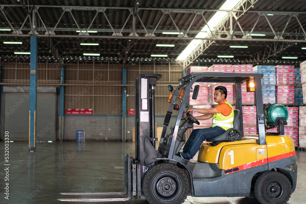 Asian male driver driving forklift to shipping delivery product in the warehouse distribution. import export logistic career, worker working at industrial factory.