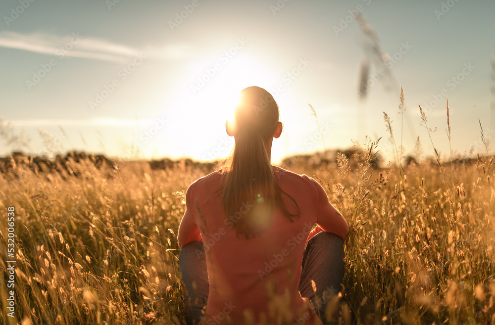 © kieferpix - Woman sitting in a meadow looking out to the sunrise with feelings of peace and happiness