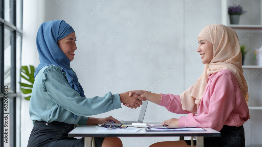 Obraz premium Beautiful Muslim Asian business woman shaking hands to promise to work together in a teamwork way.