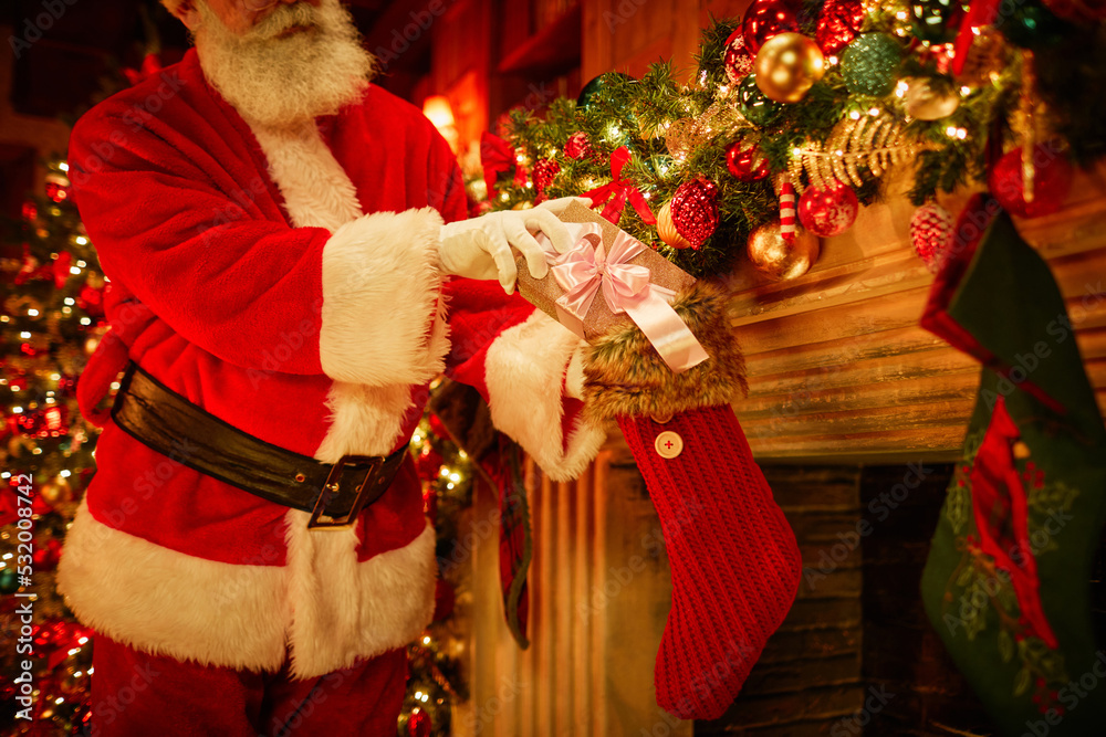Traditional Santa Claus putting present in stockings over fireplace on Christmas, copy space