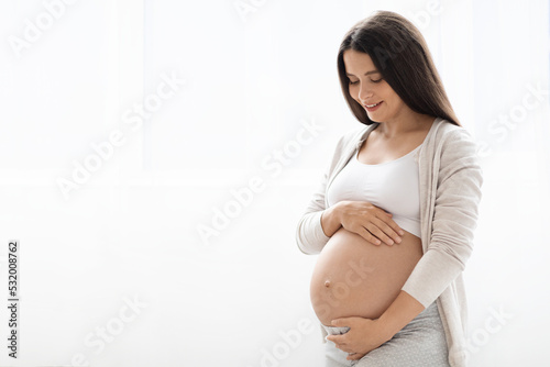 Happy pregnant woman standing next to window at home