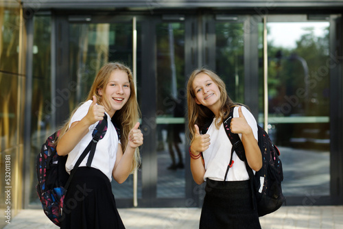 Back to school. First day of school. Two teenage girs at the entrance to the school feeling happy and excited, showing thumbs up. 