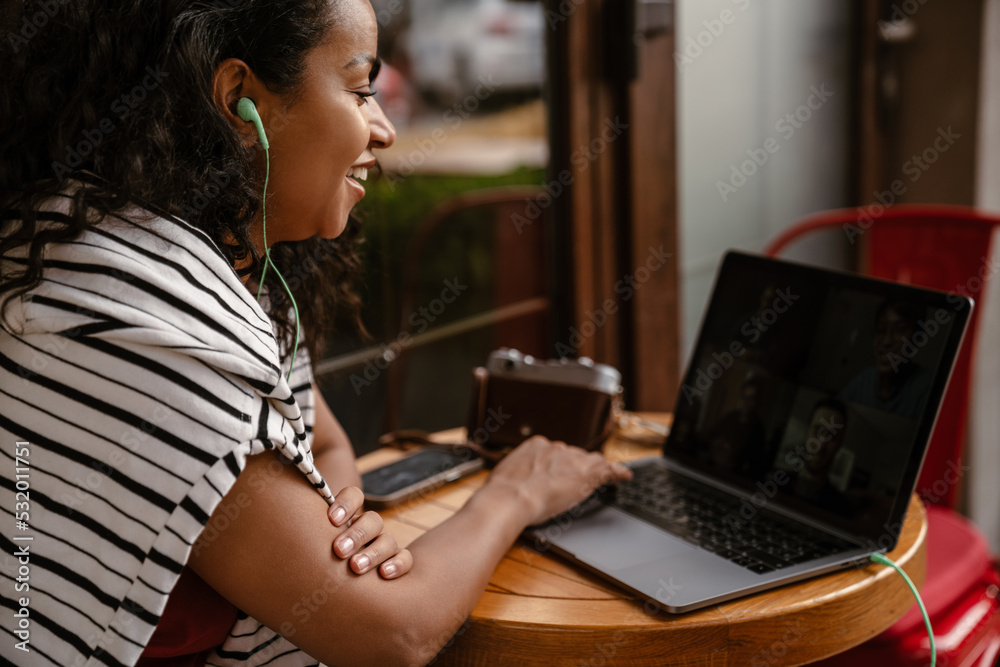 Young black woman in earphones working with laptop at cafe Young black woman in earphones working with laptop at cafe