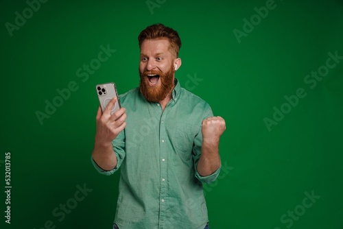 Ginger excited man in earphones playing online game on mobile phone