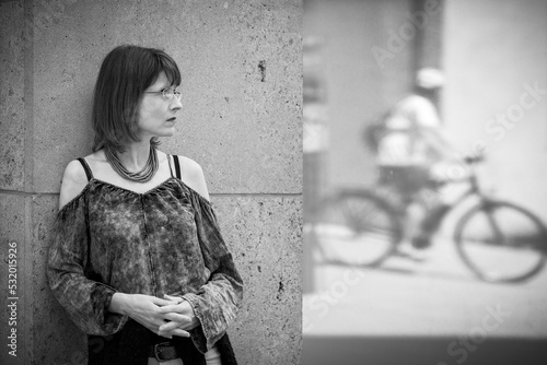 Eine hübsche Frau steht an einer Wand und beobachtet einen Fahrradfahrer, der sich im Fester spiegelt. photo