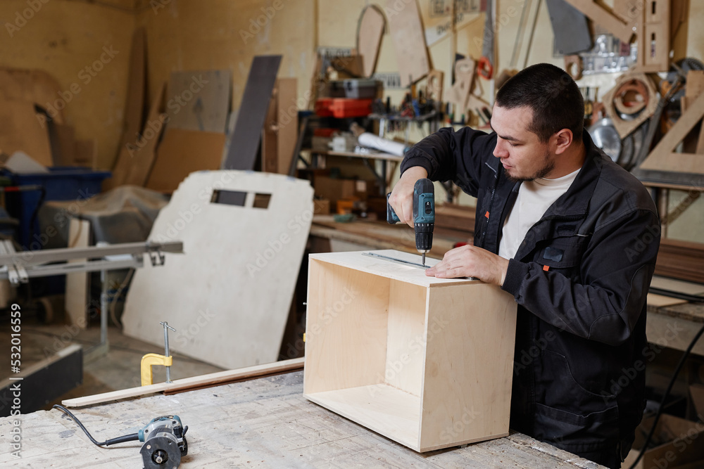 Side view portrait of male worker building wooden furniture in factory workshop, copy space